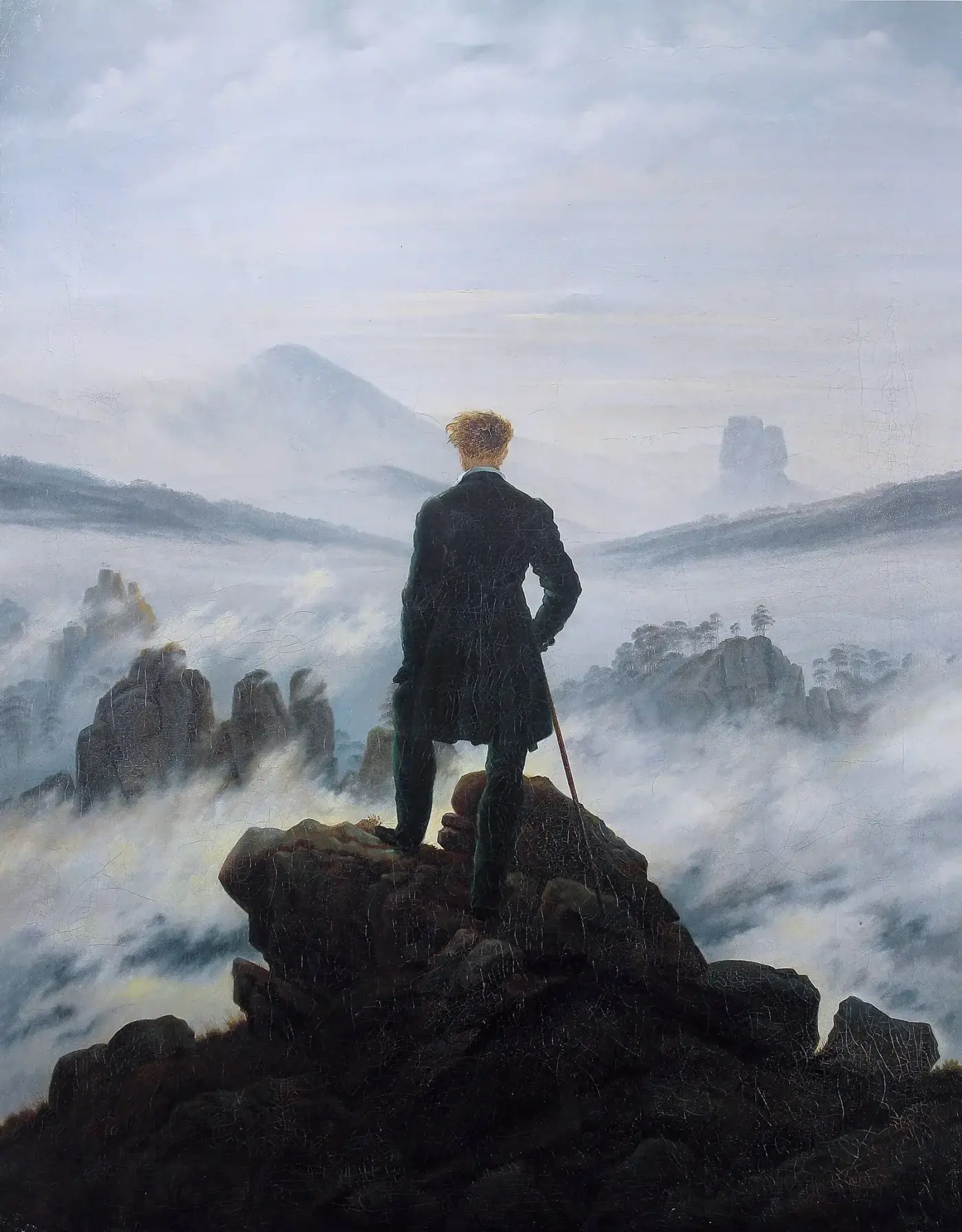 Hombre de espaldas, de pie sobre una roca, contemplando un mar de nubes del que emergen cumbres y peñascos.
