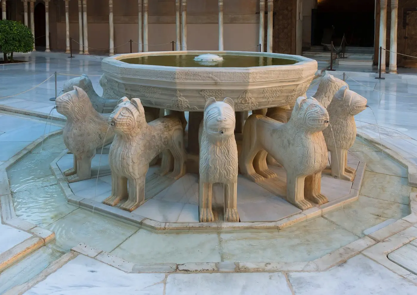 Patio nazarí con una fuente central sostenida por doce leones de piedra, rodeado de una galería de columnas finas con arcos de yesería calada.