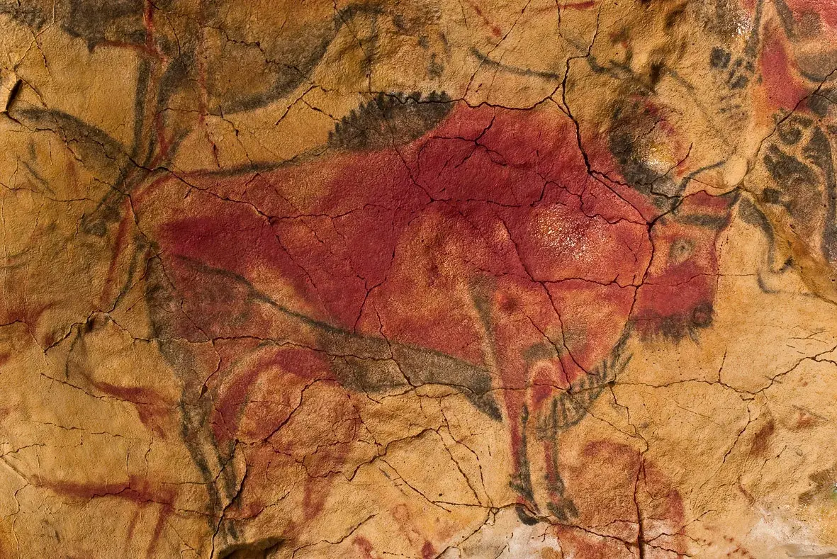 Bisonte pintado en ocres, rojos y negros sobre la roca, con la cabeza vuelta y las patas recogidas; el abultamiento natural de la roca se aprovecha para dar volumen al lomo.