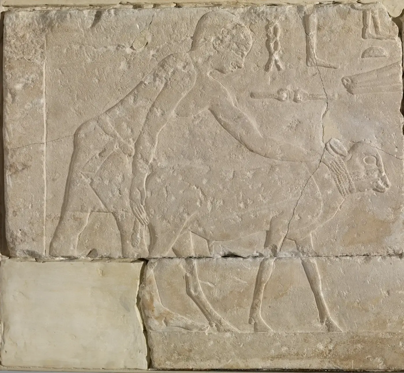 Relieve en piedra caliza con una figura masculina caminando: cabeza de perfil con el ojo de frente, hombros y torso de frente, caderas y piernas de perfil.