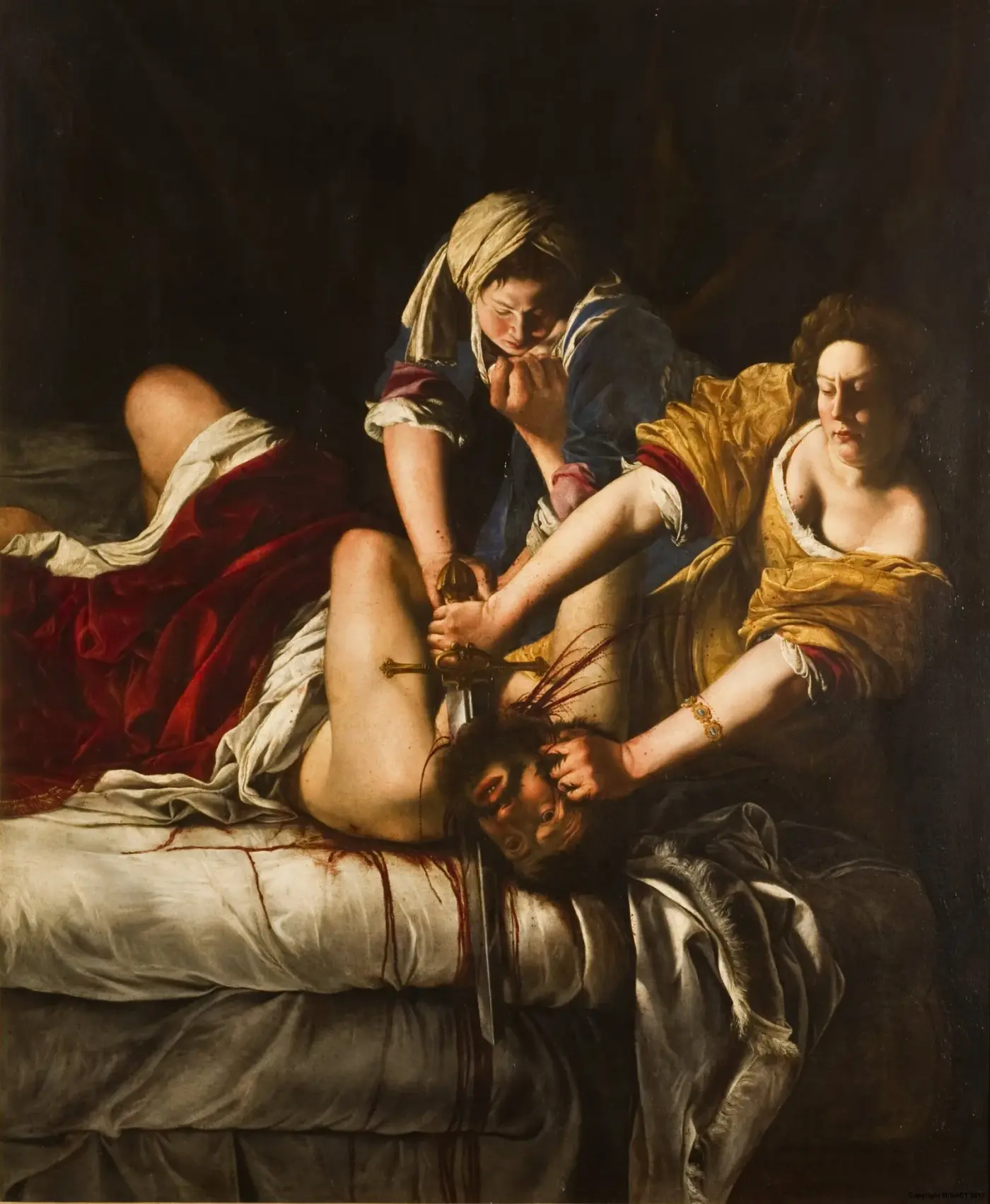 Dos mujeres sujetan a un hombre sobre un lecho mientras una de ellas le corta el cuello con una espada; la escena está iluminada por un foco lateral que deja el fondo en penumbra.